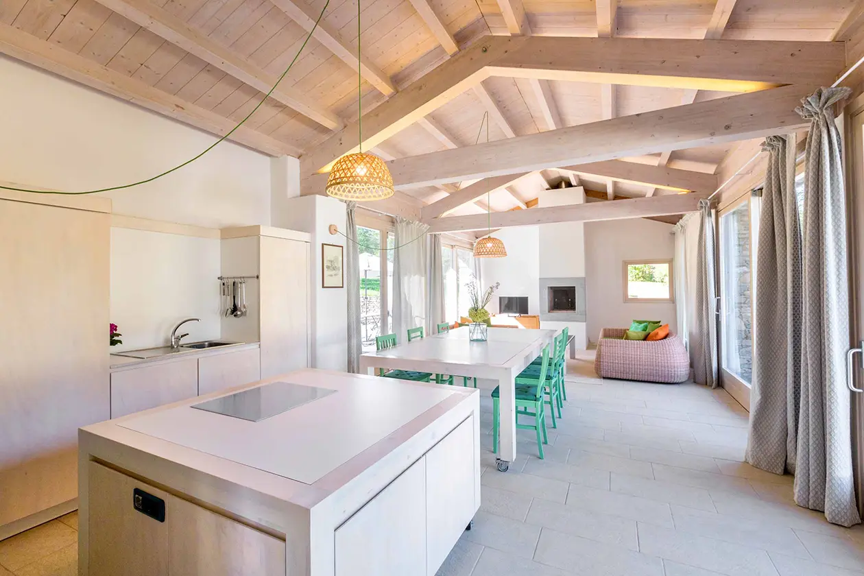 Zona giorno dell’appartamento Il Mulino nella cascina storica del Castello di Bagnolo, con cucina, grande tavolo e soffitto in legno a vista.
