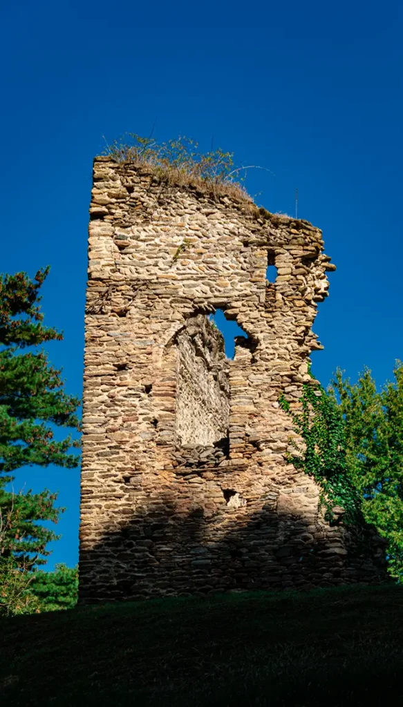 Rudere medievale in pietra su prato, con apertura muraria irregolare e vegetazione circostante sotto cielo azzurro.