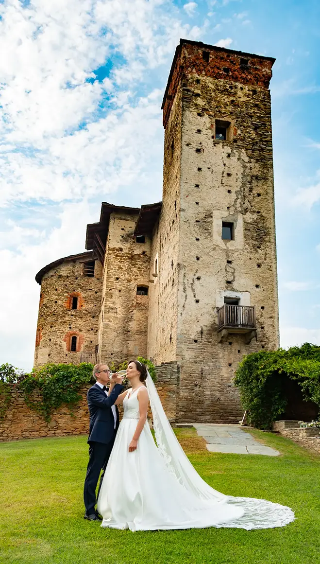 Sposi nel prato davanti alla torre quadrangolare in pietra del Castello medievale.