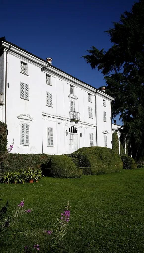 Facciata bianca del palazzo storico del Castello di Bagnolo Piemonte affacciata sul parco con prato e alberi