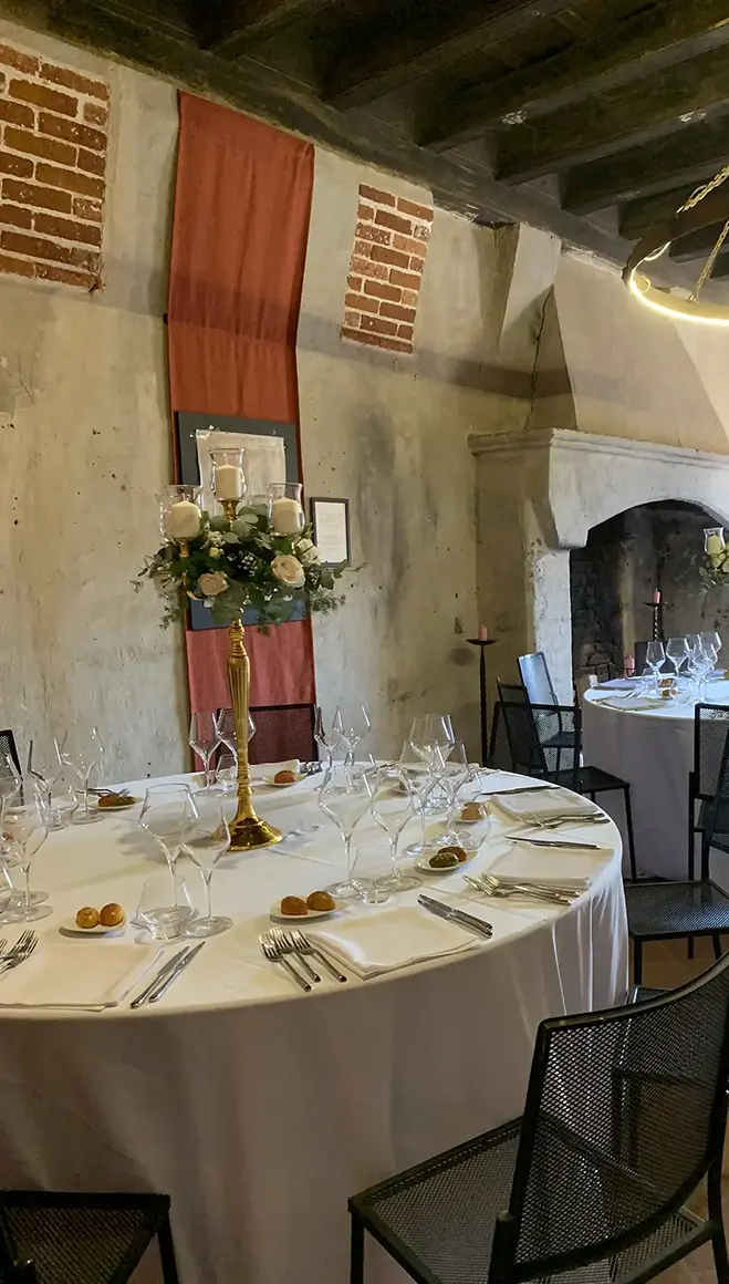 Tavolo rotondo allestito in una sala del Castello con pareti materiche, inserti in laterizio e camino in pietra.