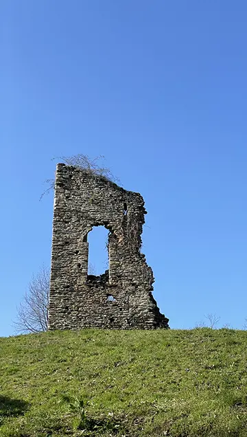 Rudere in pietra con apertura verticale su collina erbosa sotto cielo azzurro